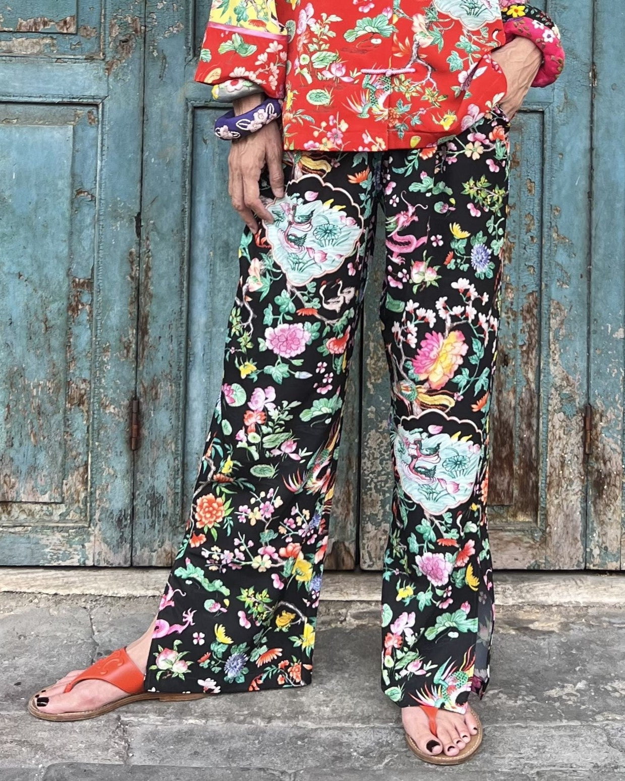 Person wearing colorful floral pants and jacket in front of a rustic wooden door.