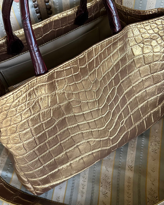 Gold textured handbag with dark handles on a striped fabric background