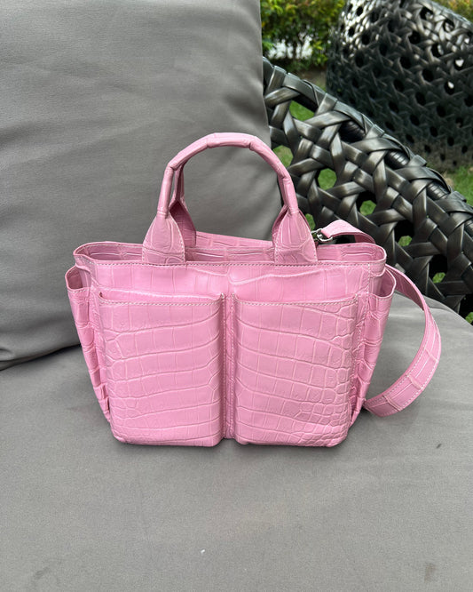 Pink handbag with crocodile pattern on a gray surface