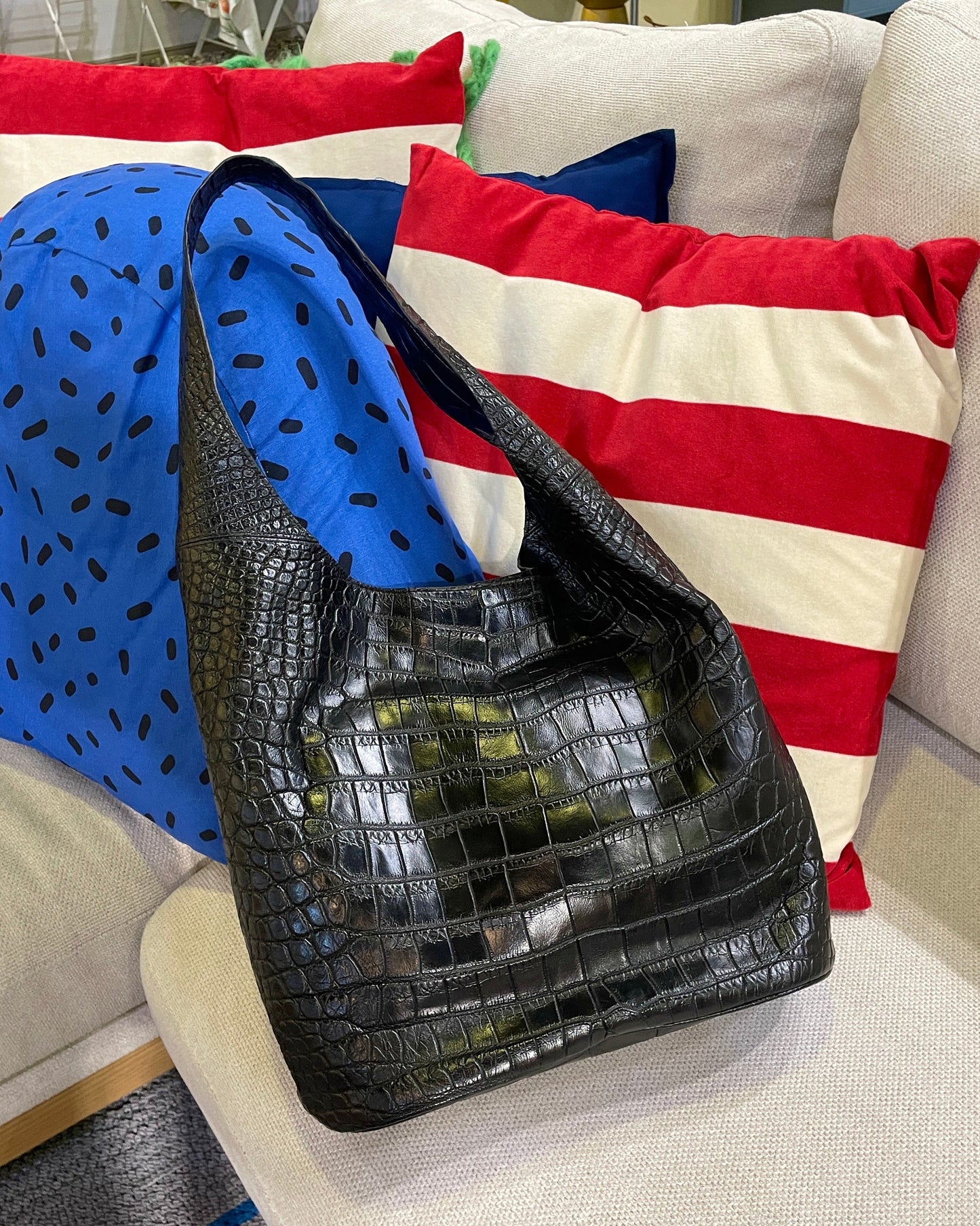 Black crocodile-patterned handbag on a beige couch with colorful pillows