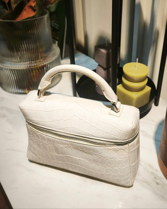 White handbag on a white surface with plants and a black metal shelf in the background
