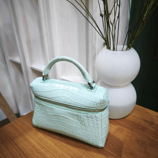 Light blue handbag on a wooden surface with a white vase and branches in the background.