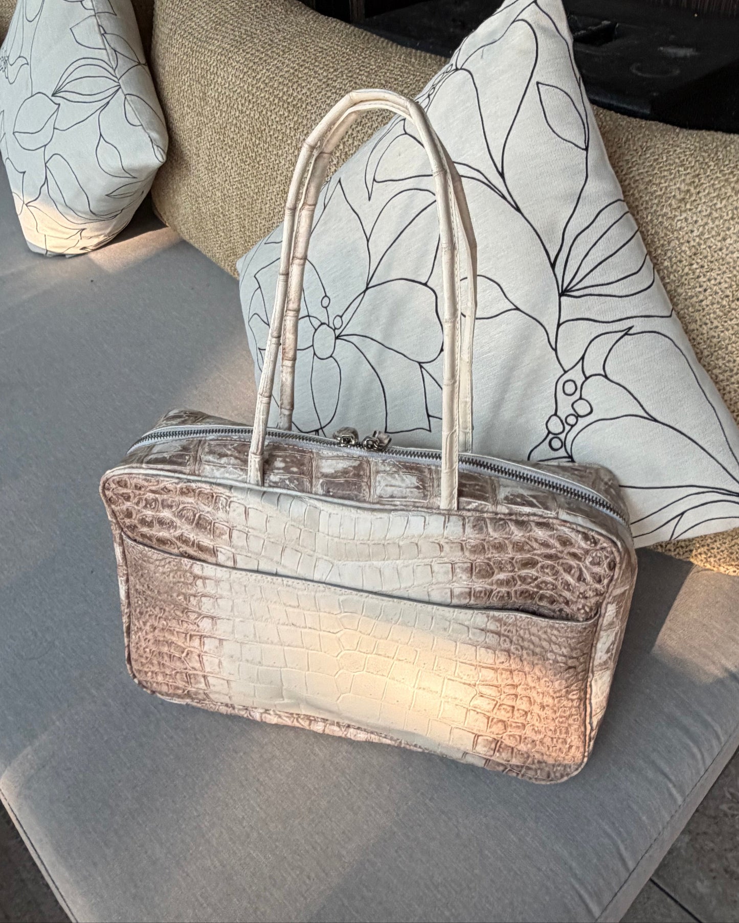 Brown textured handbag on a gray surface with decorative pillows in the background