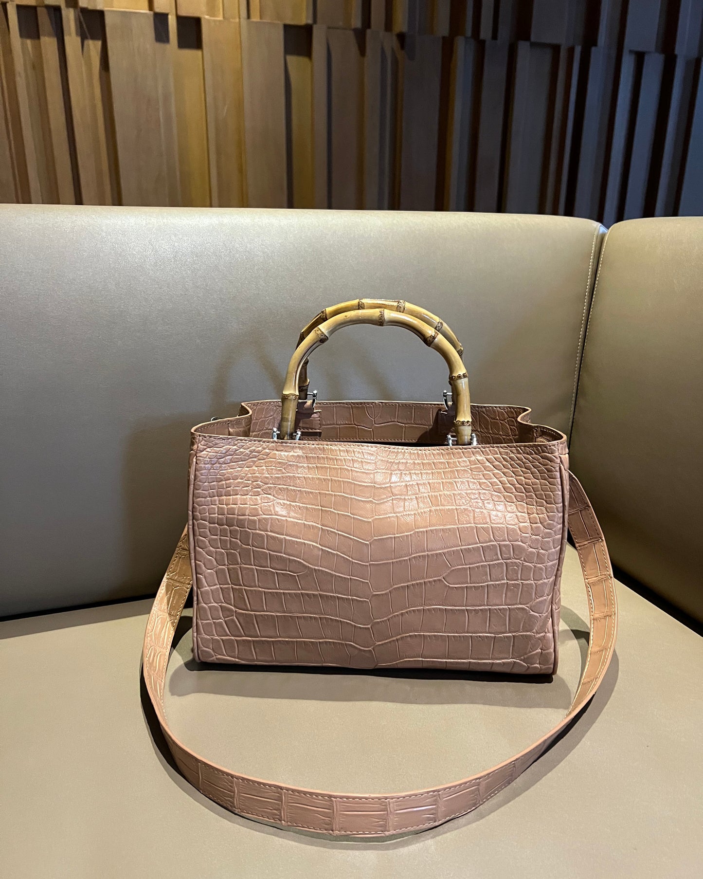 Beige textured handbag with gold handle and strap on a neutral background