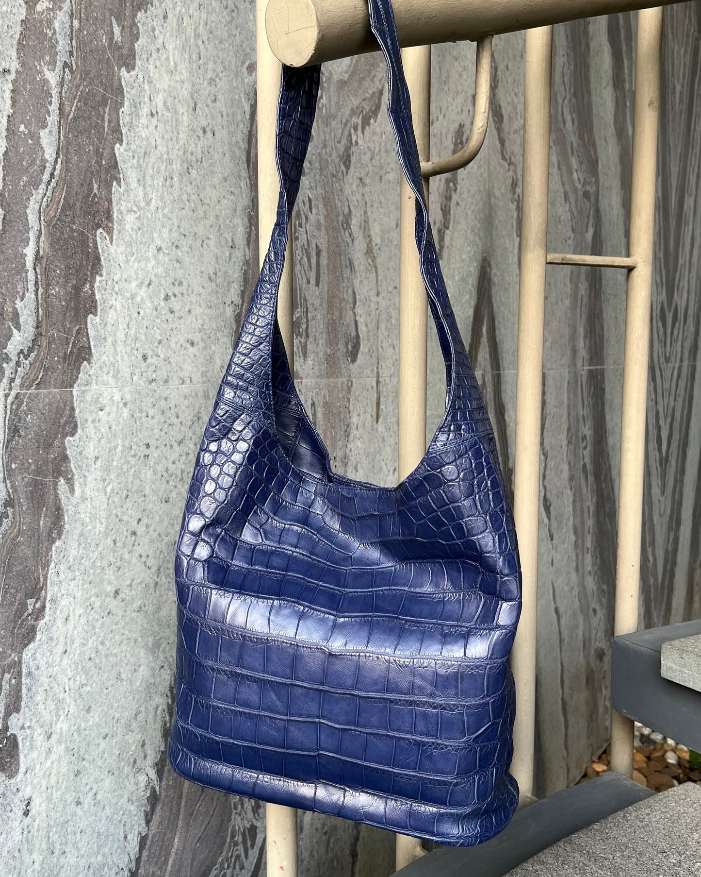 Blue textured handbag hanging on a wooden chair against a stone wall.