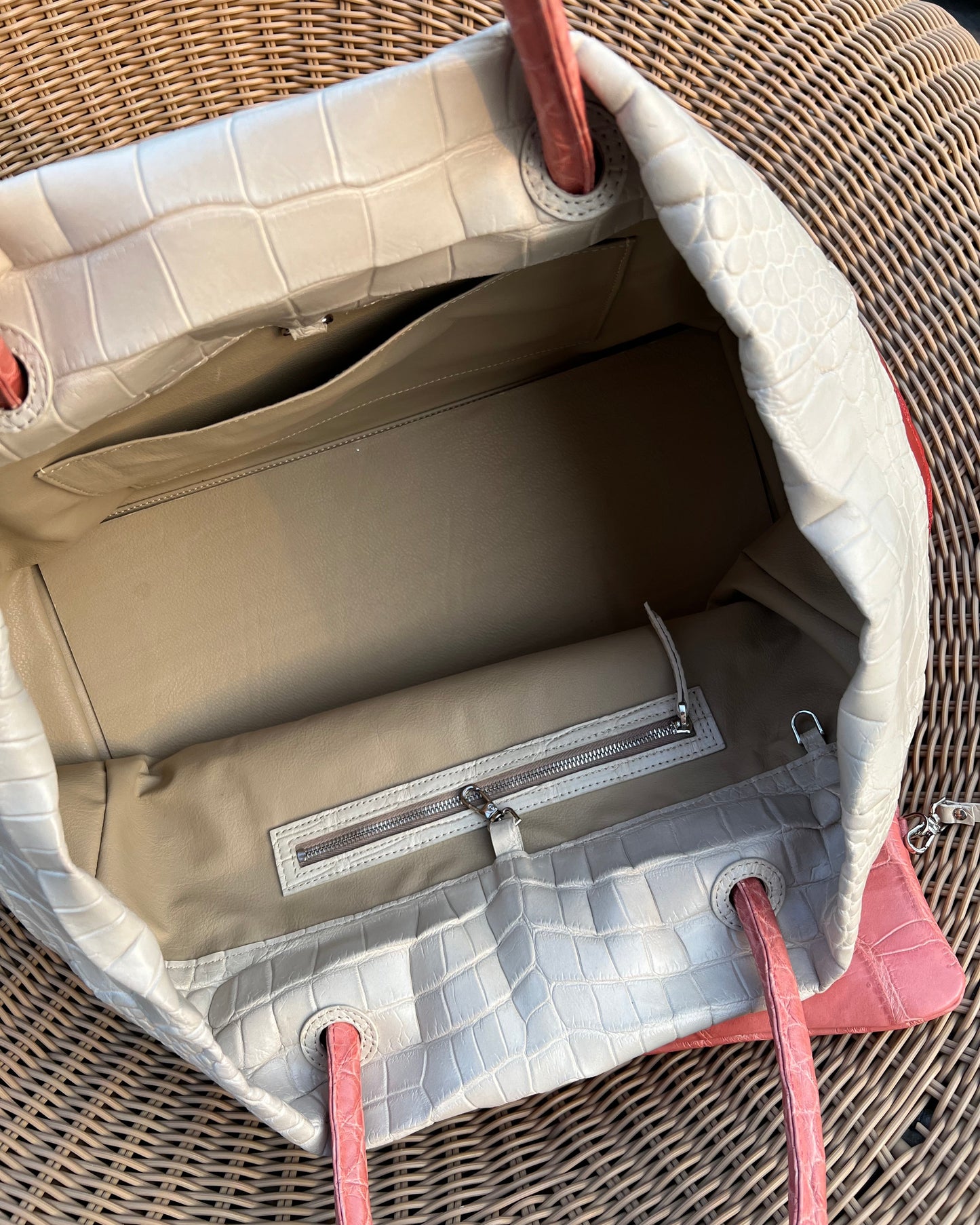 Close-up of a beige and red handbag with a textured surface on a wicker surface.
