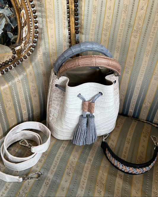 White woven bag with brown handle and tassel on a striped surface