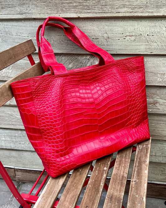 Red textured tote bag on a wooden chair against a wooden wall.