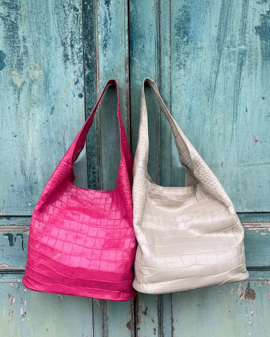 Two handbags, one pink and one beige, leaning against a textured blue wall.