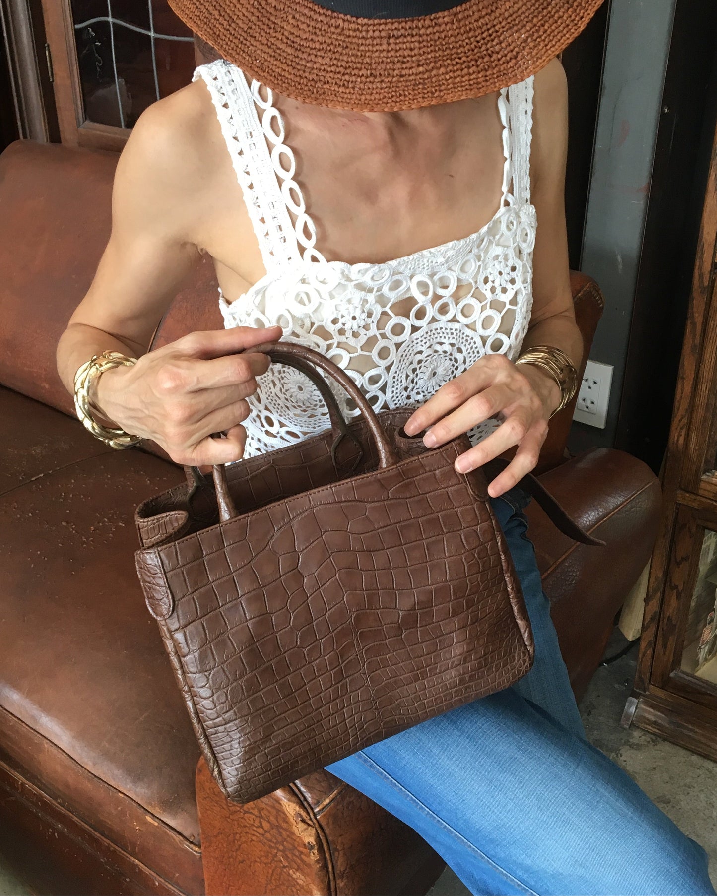 Person sitting on a brown leather chair holding a brown leather handbag.