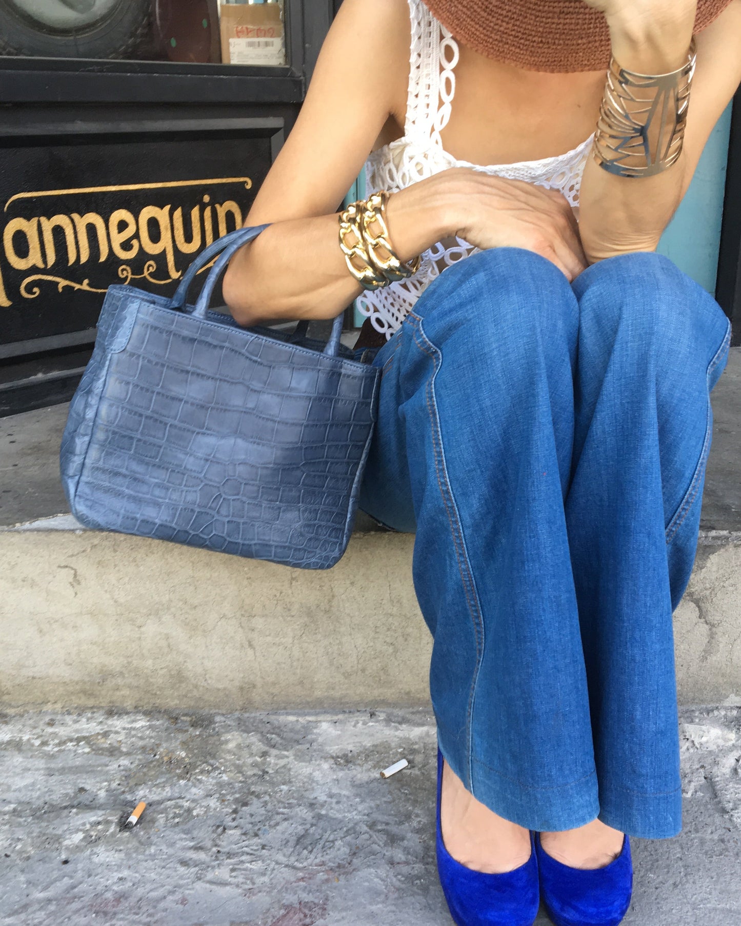 Person wearing blue jeans and white lace top sitting on a curb.