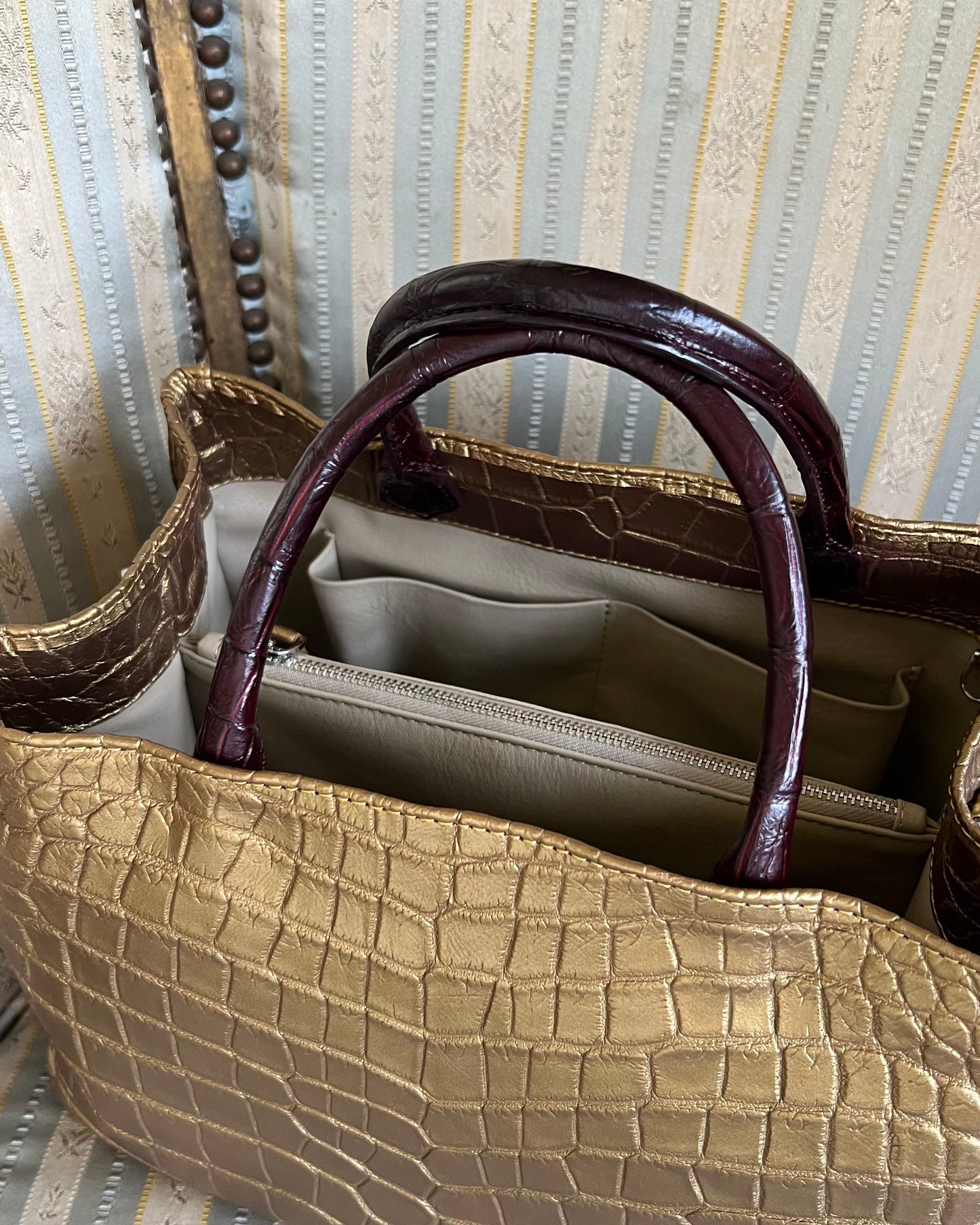 Gold textured handbag with dark brown handles on a striped chair.