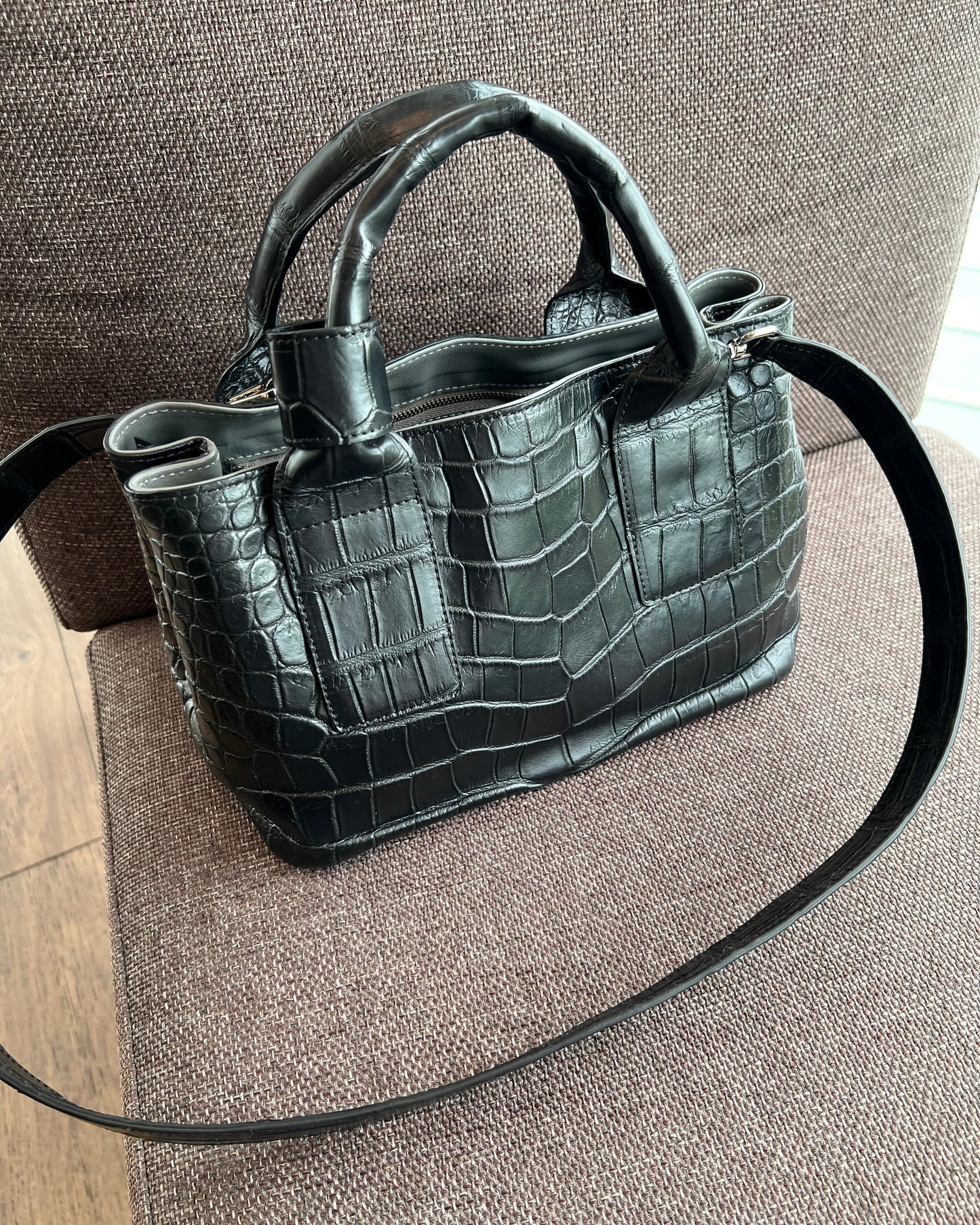 Black crocodile-patterned handbag on a brown textured surface