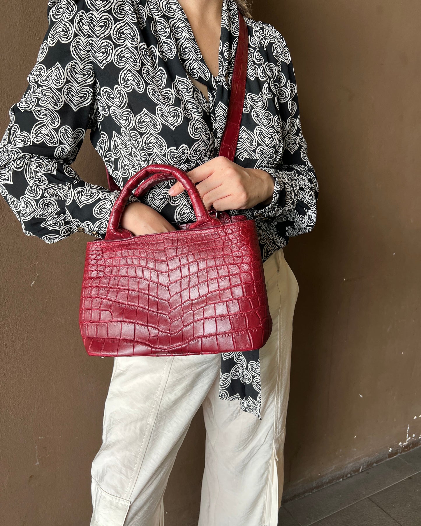 Person holding a red handbag with a patterned dress and white pants.