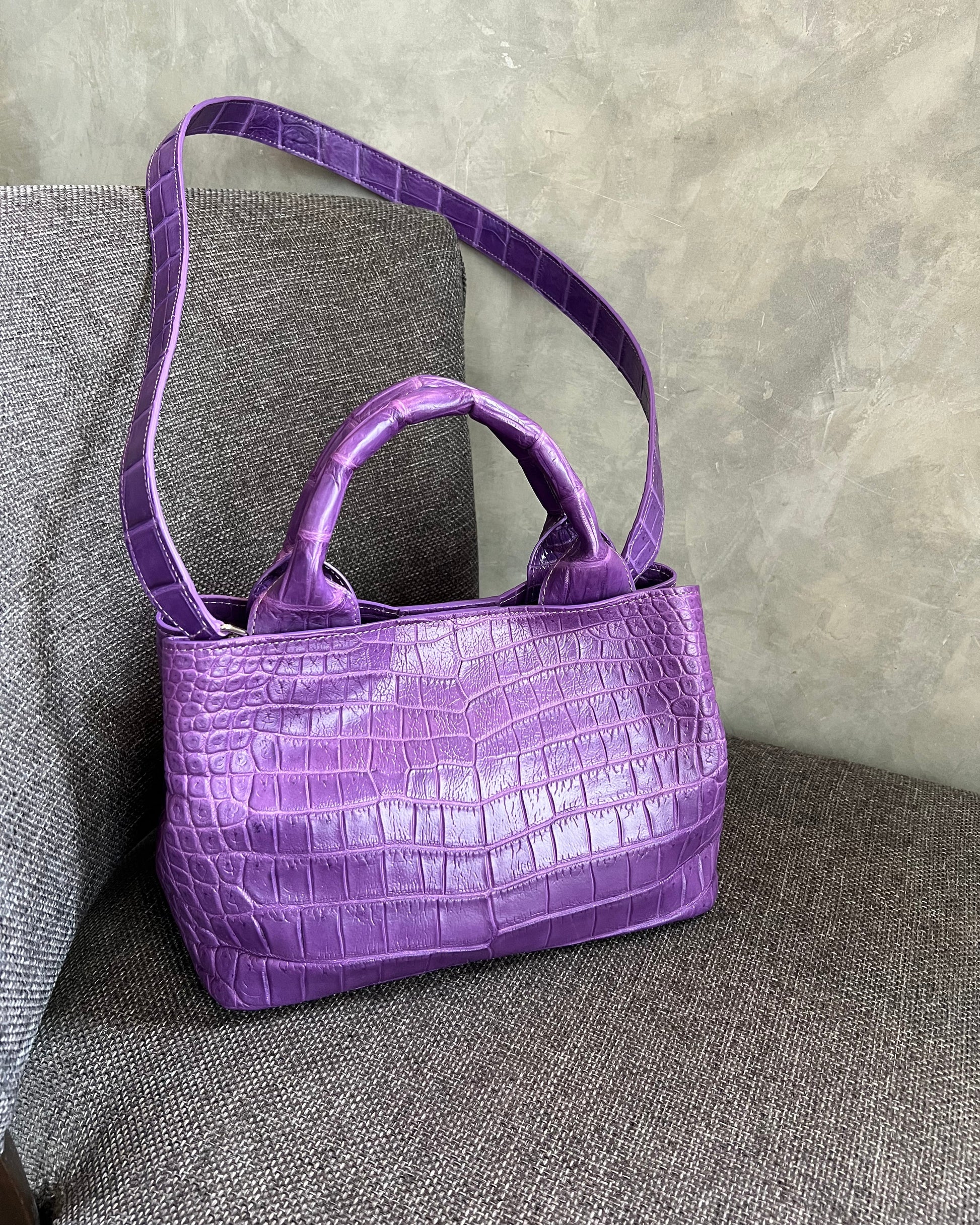 Purple crocodile-patterned handbag on a gray surface