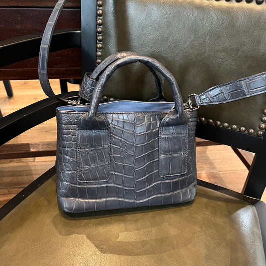 Black crocodile-patterned handbag on a chair with a blurred background