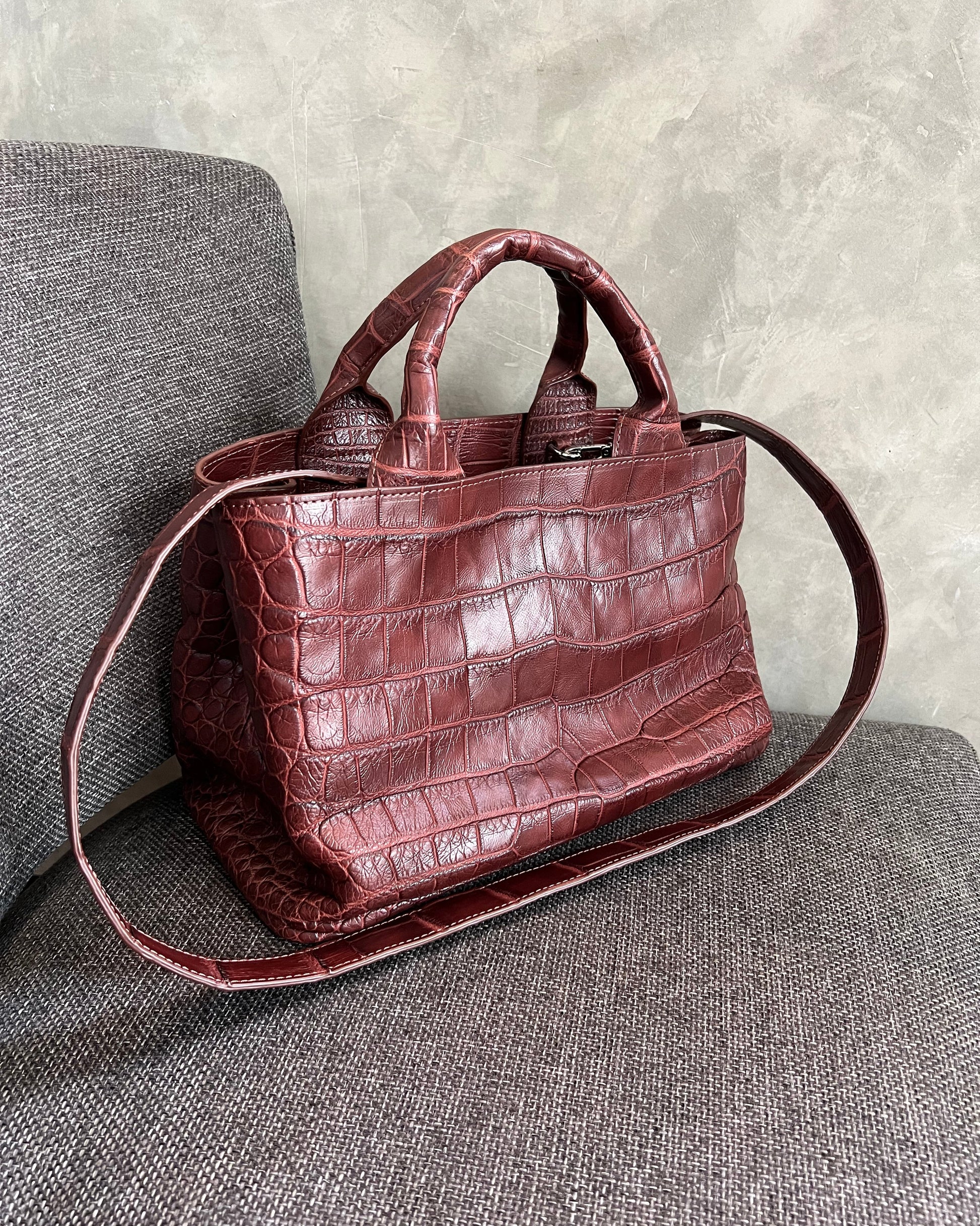 Brown crocodile-patterned handbag on a gray surface