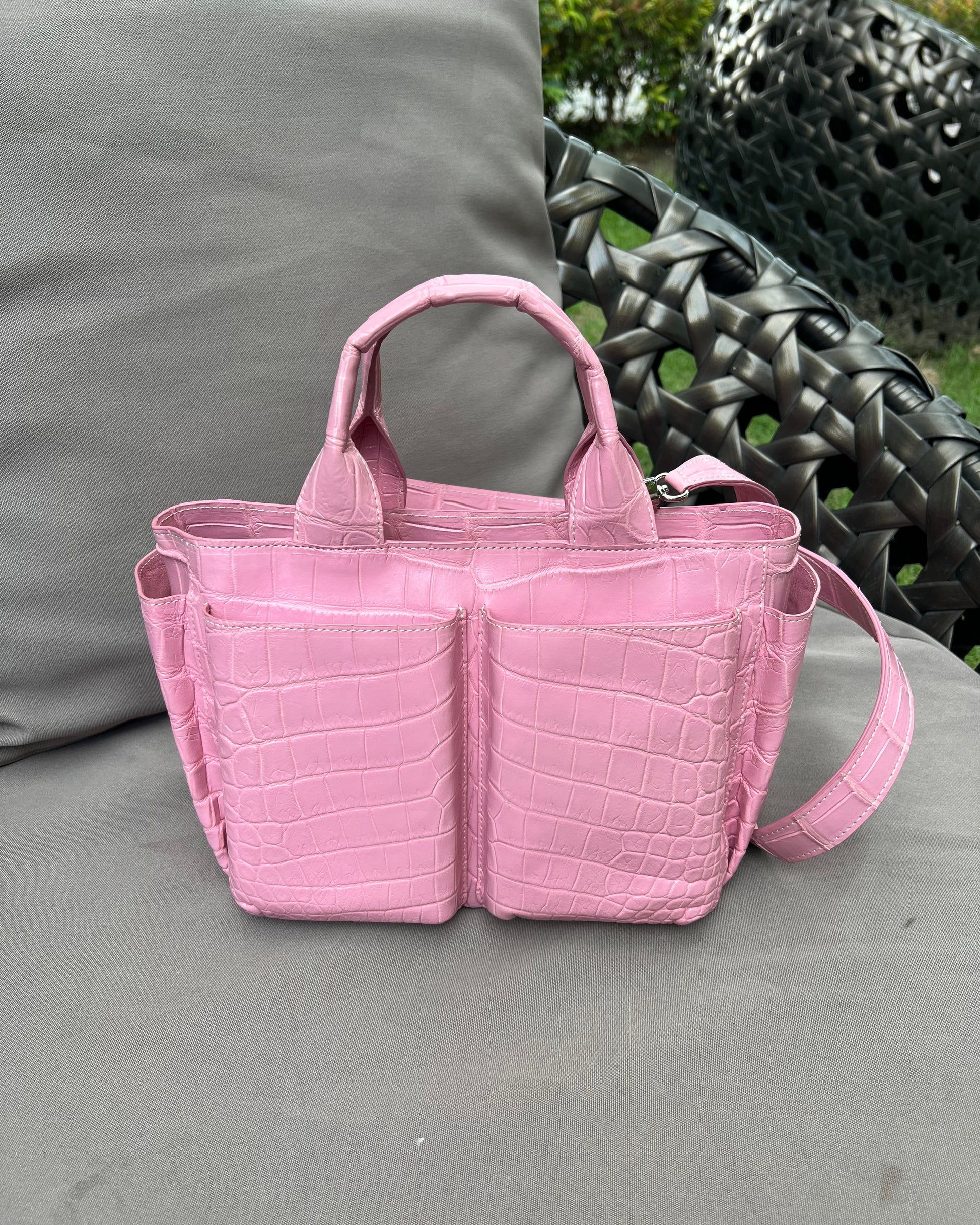Pink handbag with crocodile pattern on a gray surface