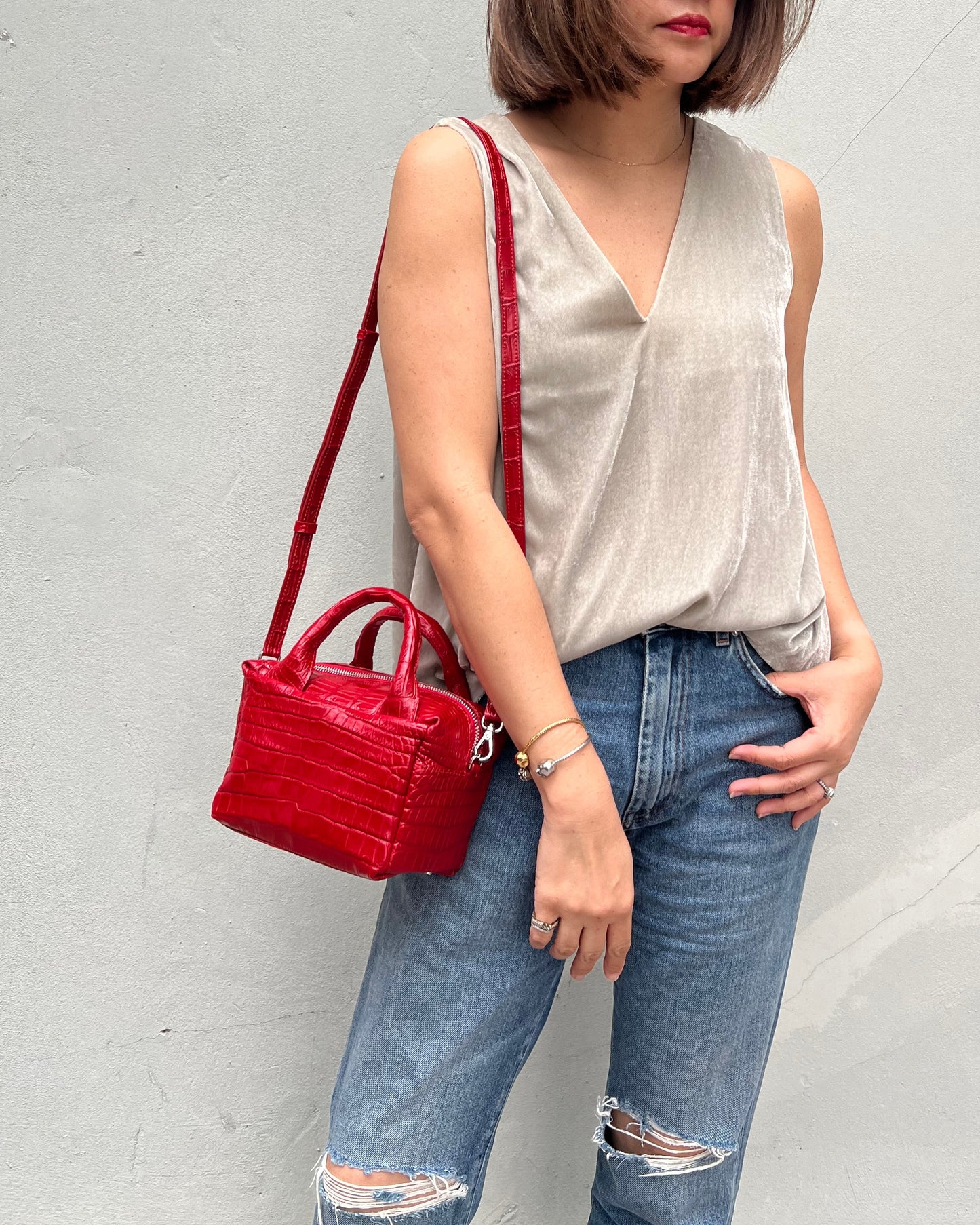 Person wearing a gray top and blue jeans, holding a red handbag on a light gray background