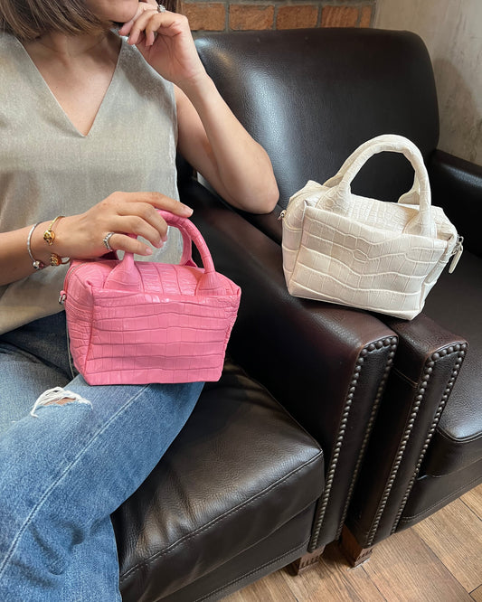 Person holding a pink handbag with another handbag on a chair in the background.