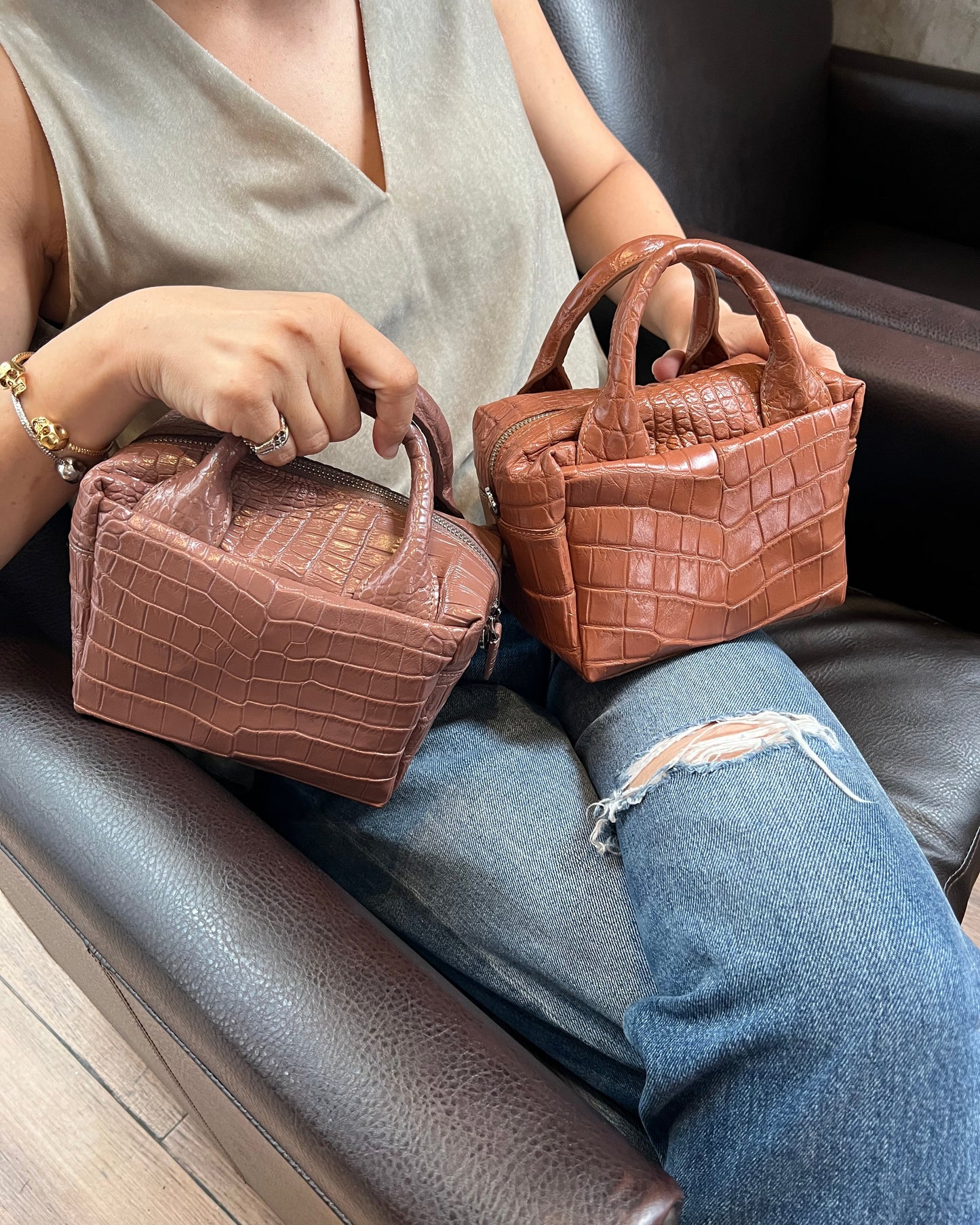 Two brown textured handbags held by a person sitting on a chair.