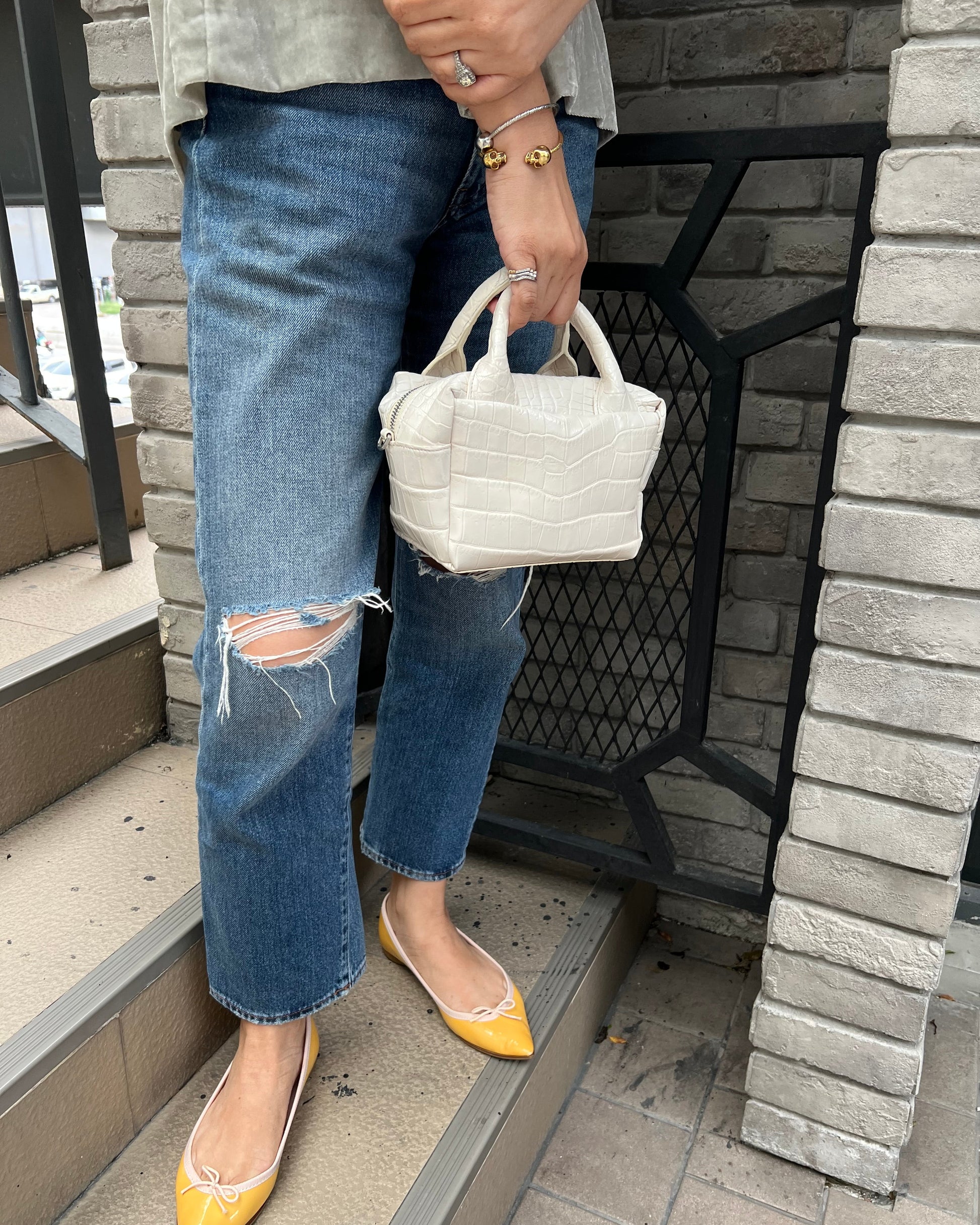 Person holding a white woven handbag wearing blue jeans and yellow shoes on a stone staircase.