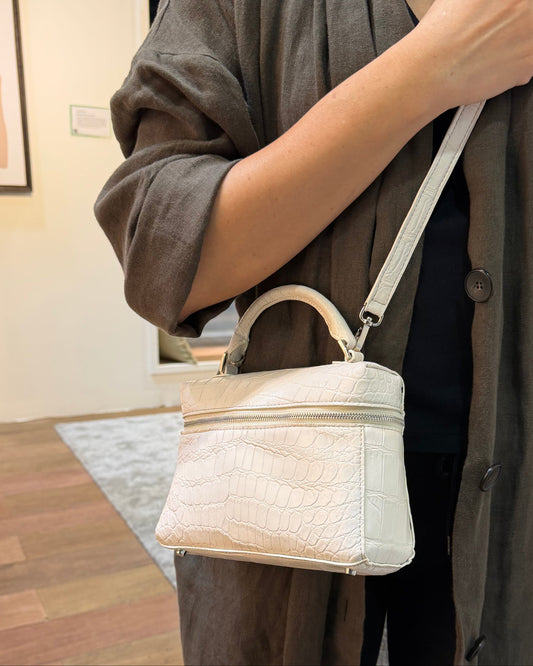 Person holding a beige handbag in a room with wooden flooring and a mirror.