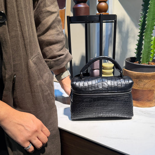 Person wearing brown coat with a black handbag standing next to a cactus plant.