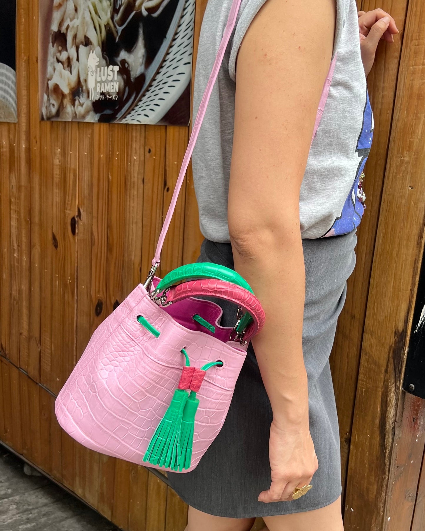 Person holding a pink handbag with green accents against a wooden wall.