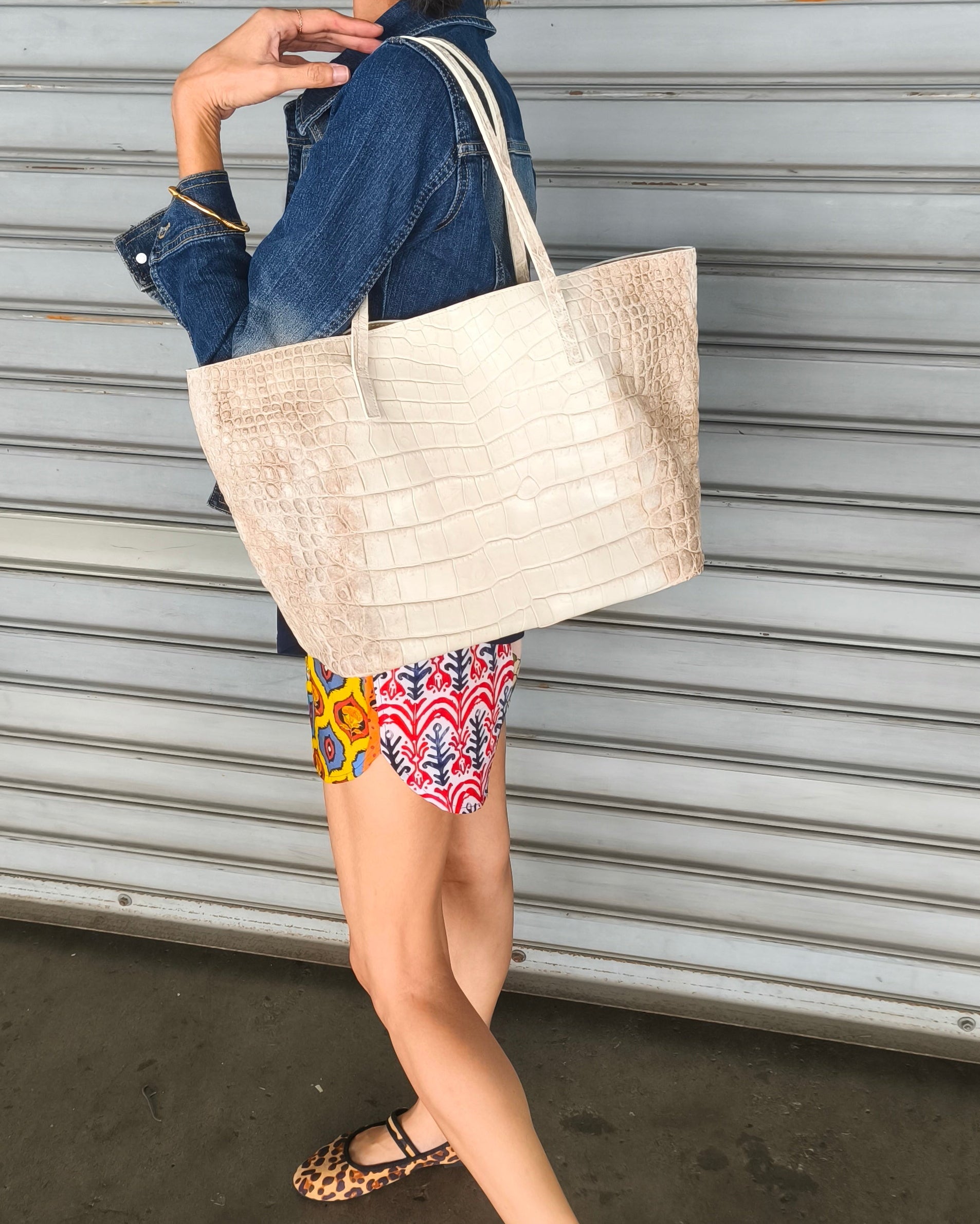 Woman carrying a beige tote bag against a metallic shutter background