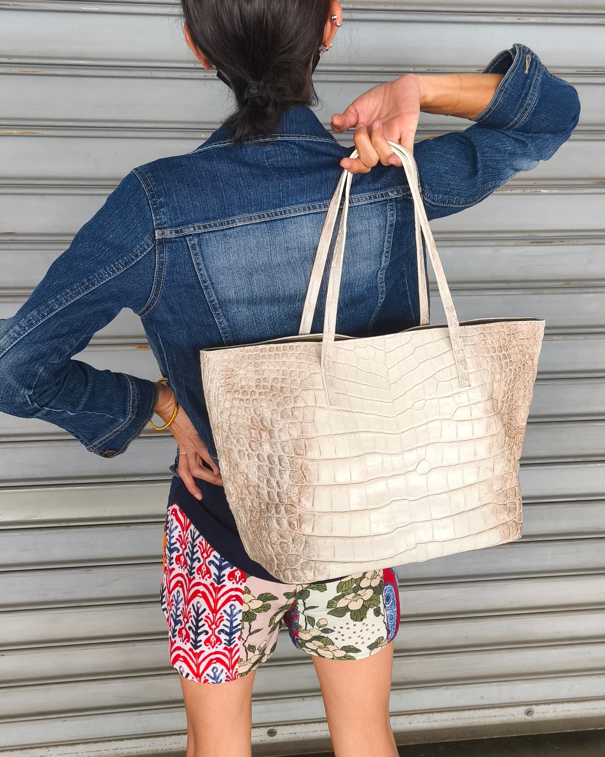 Person holding a beige tote bag in front of a metallic shutter.