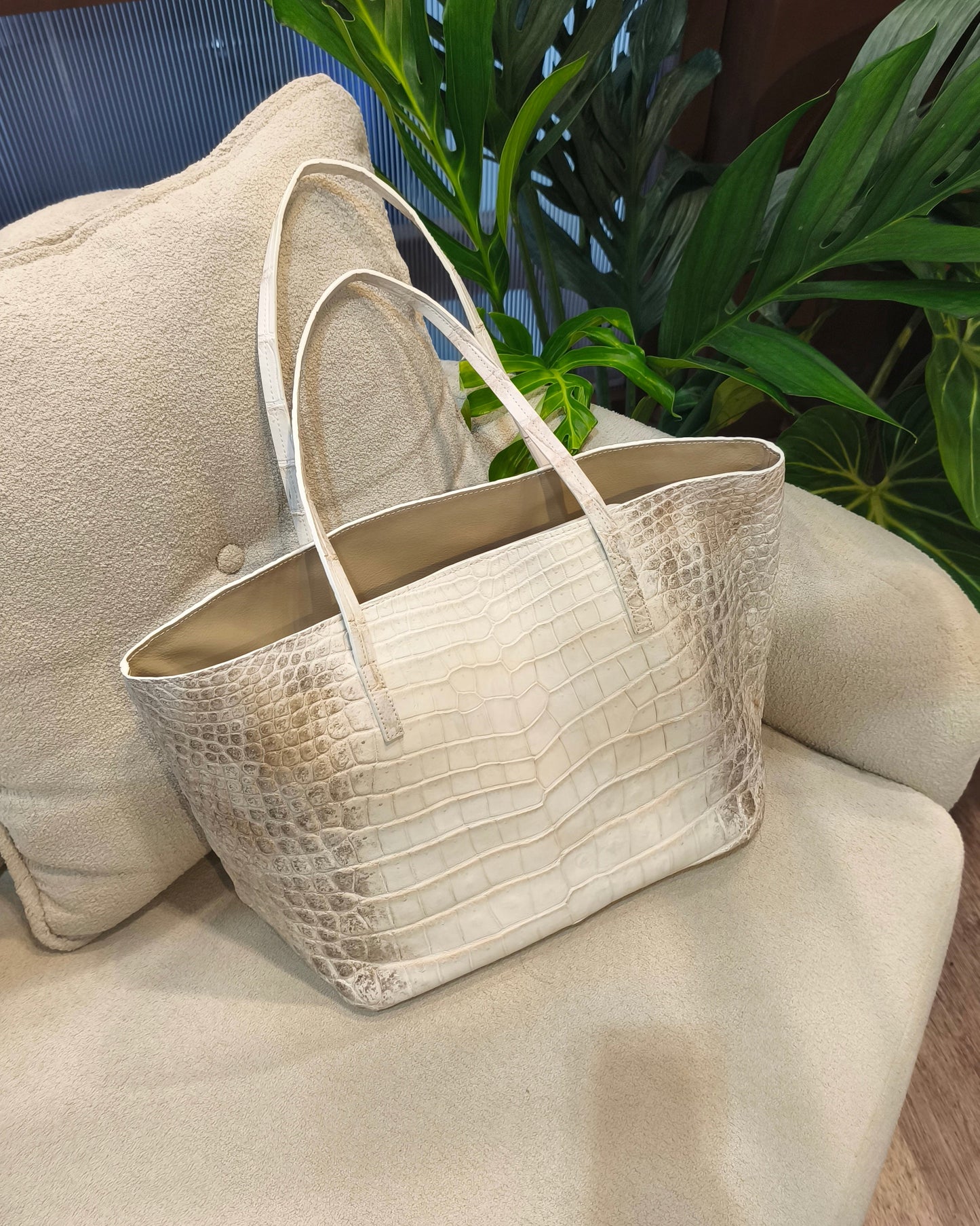 Beige handbag on a beige sofa with plants in the background