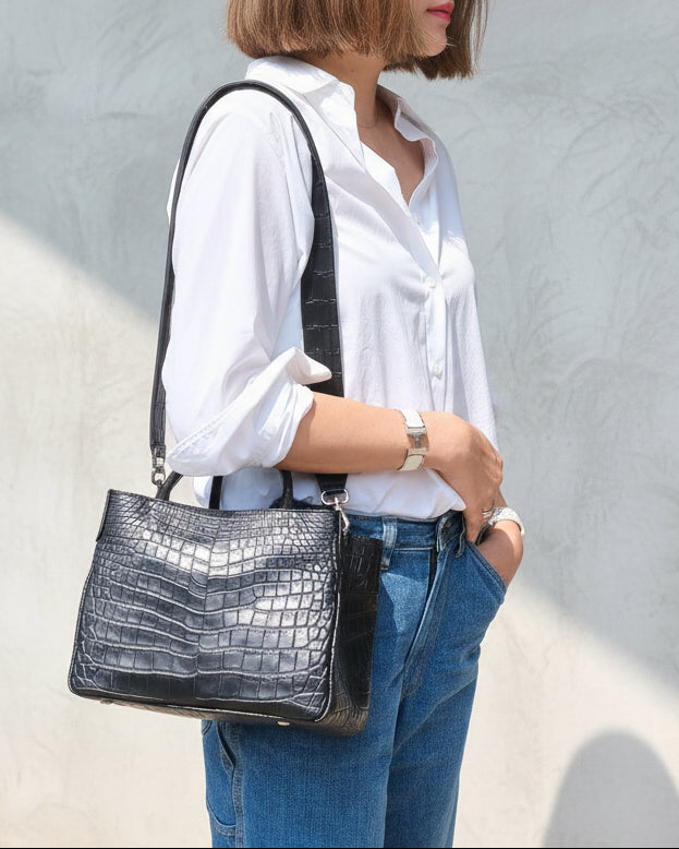 Woman in white shirt and blue shorts holding a black handbag outdoors.
