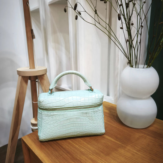Light blue handbag on a wooden surface with a white vase and decorative branches in the background.