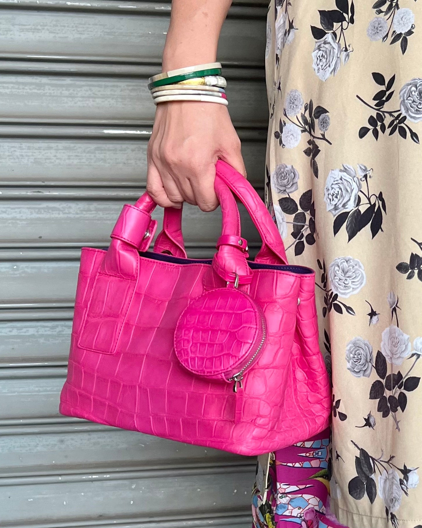 Person holding a pink handbag with a floral dress in the background