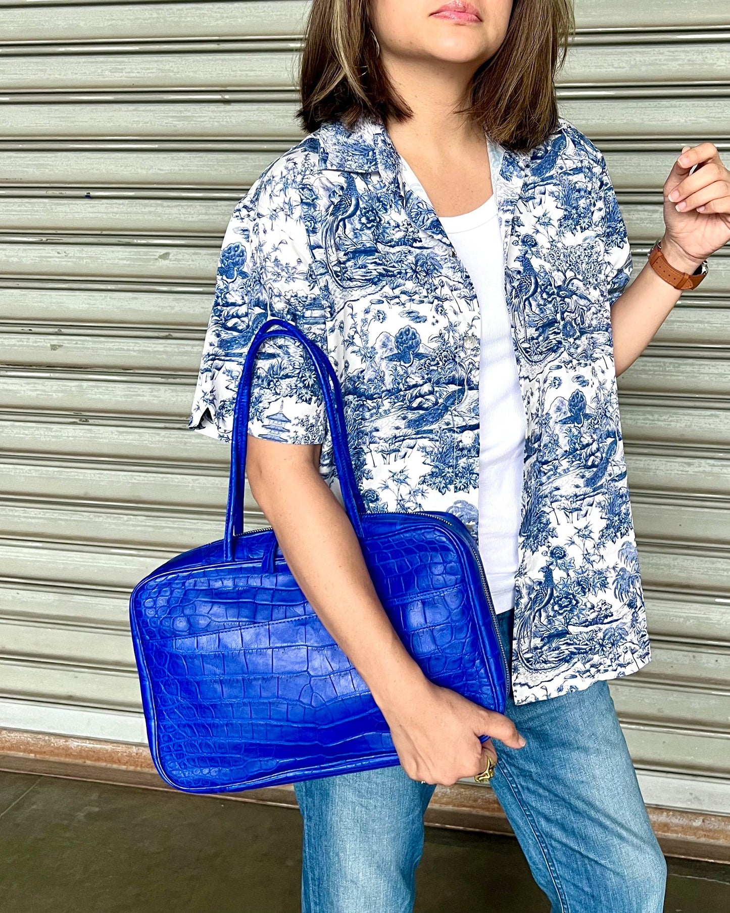 Woman holding a blue handbag in front of a metallic shutter.