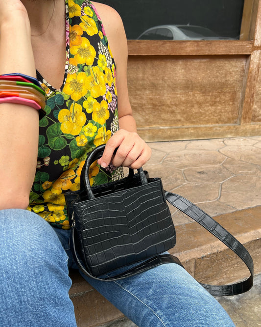 Person holding a black handbag with floral skirt and colorful bracelets in foreground