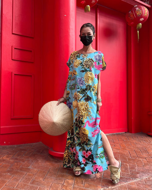 Woman in a floral dress holding a hat against a red wall.