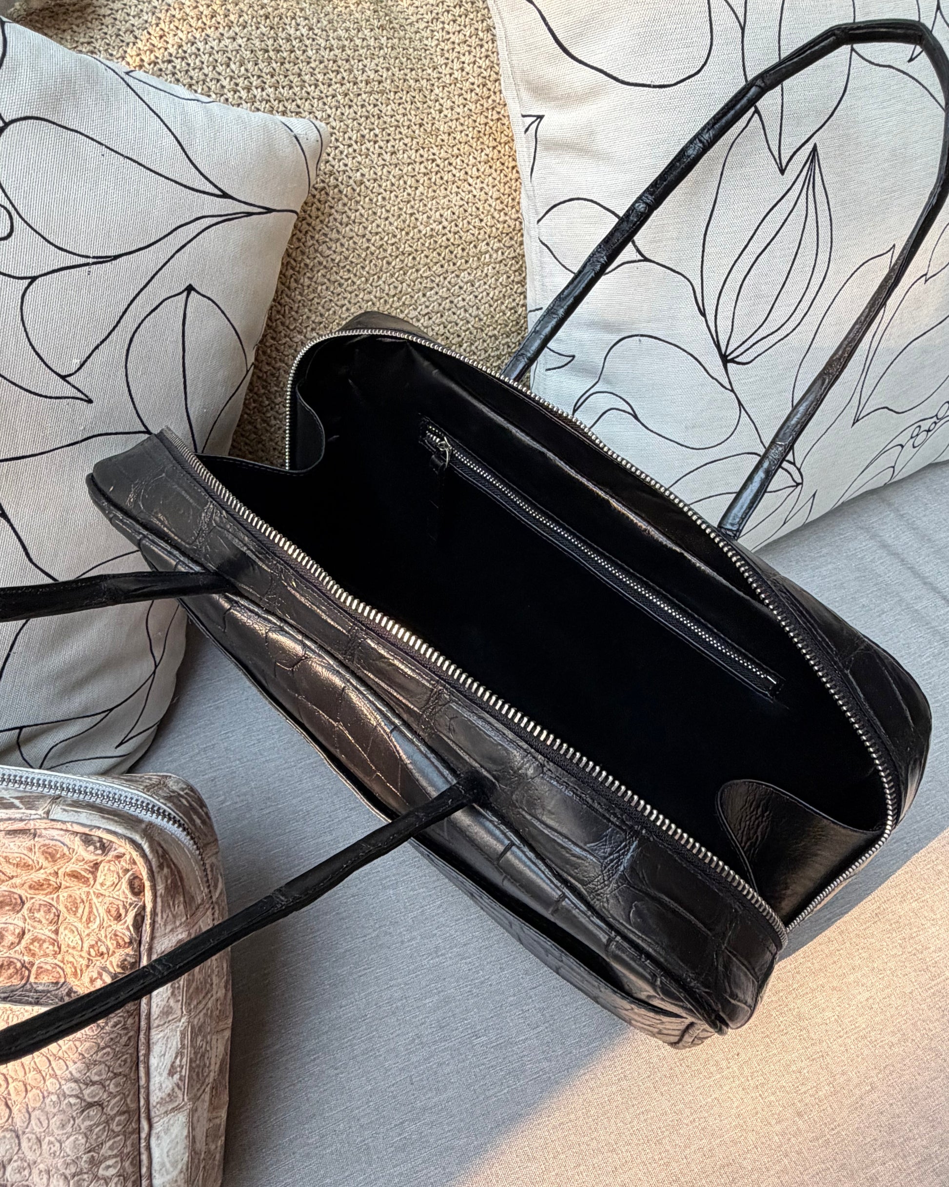 Black leather handbag on a textured surface with pillows in the background