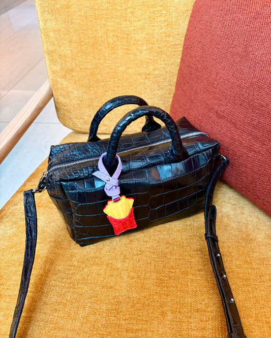 Black handbag with a colorful keychain on a yellow chair