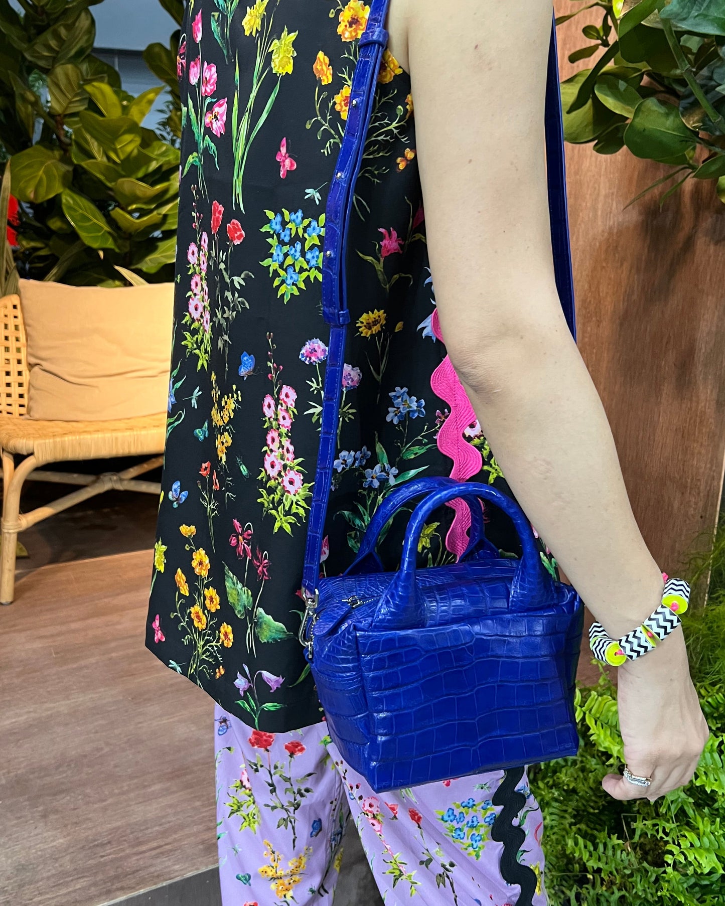 Person holding a blue handbag with floral-patterned bag carrier, surrounded by greenery.
