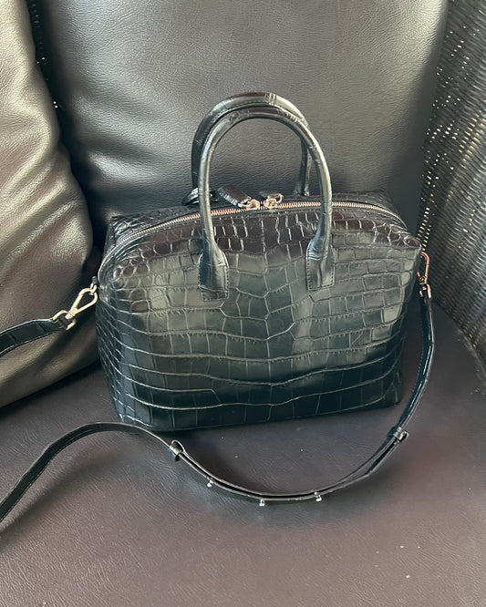 Black crocodile-patterned handbag on a dark textured surface