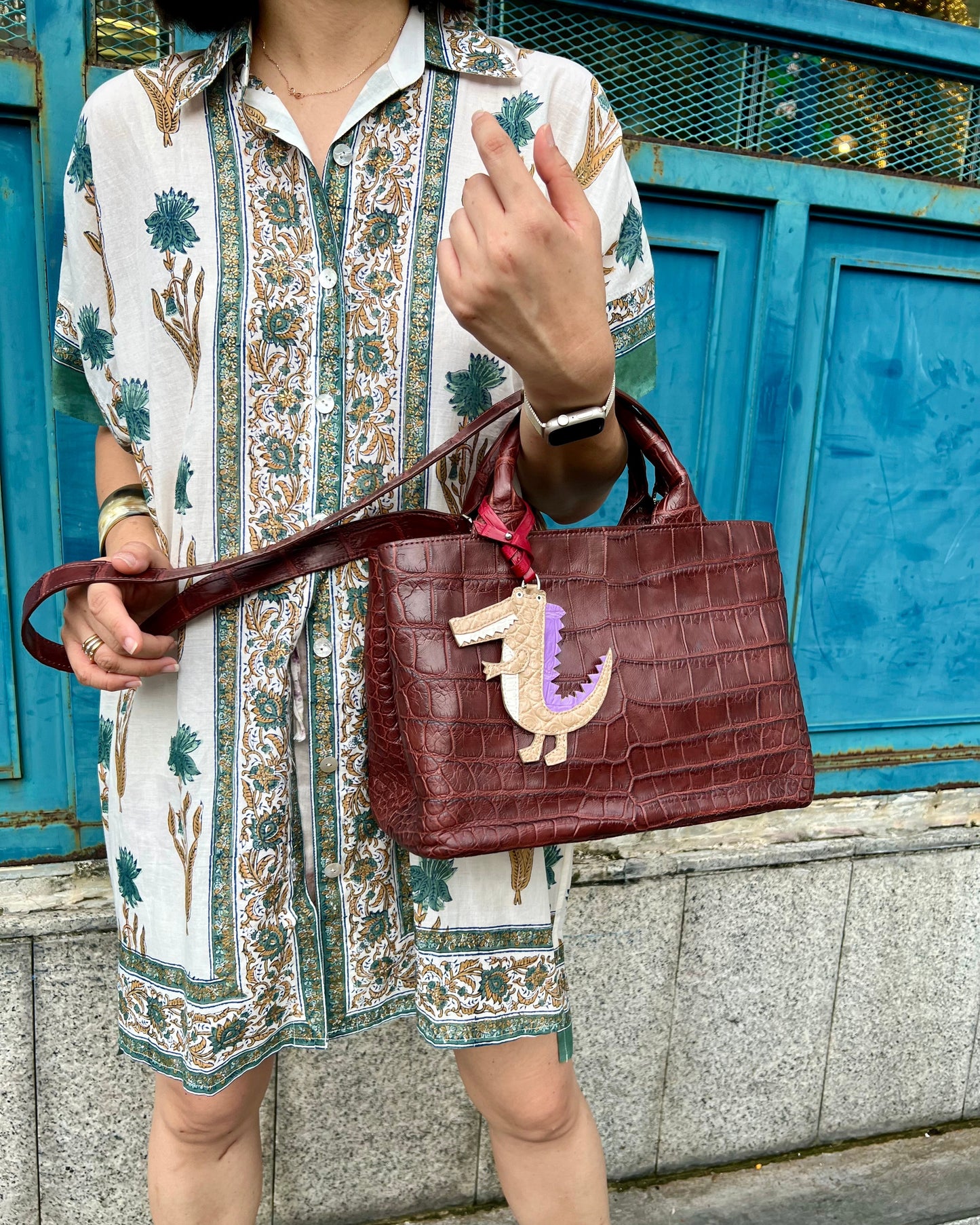 Person holding a maroon handbag with a character design against a blue wall.