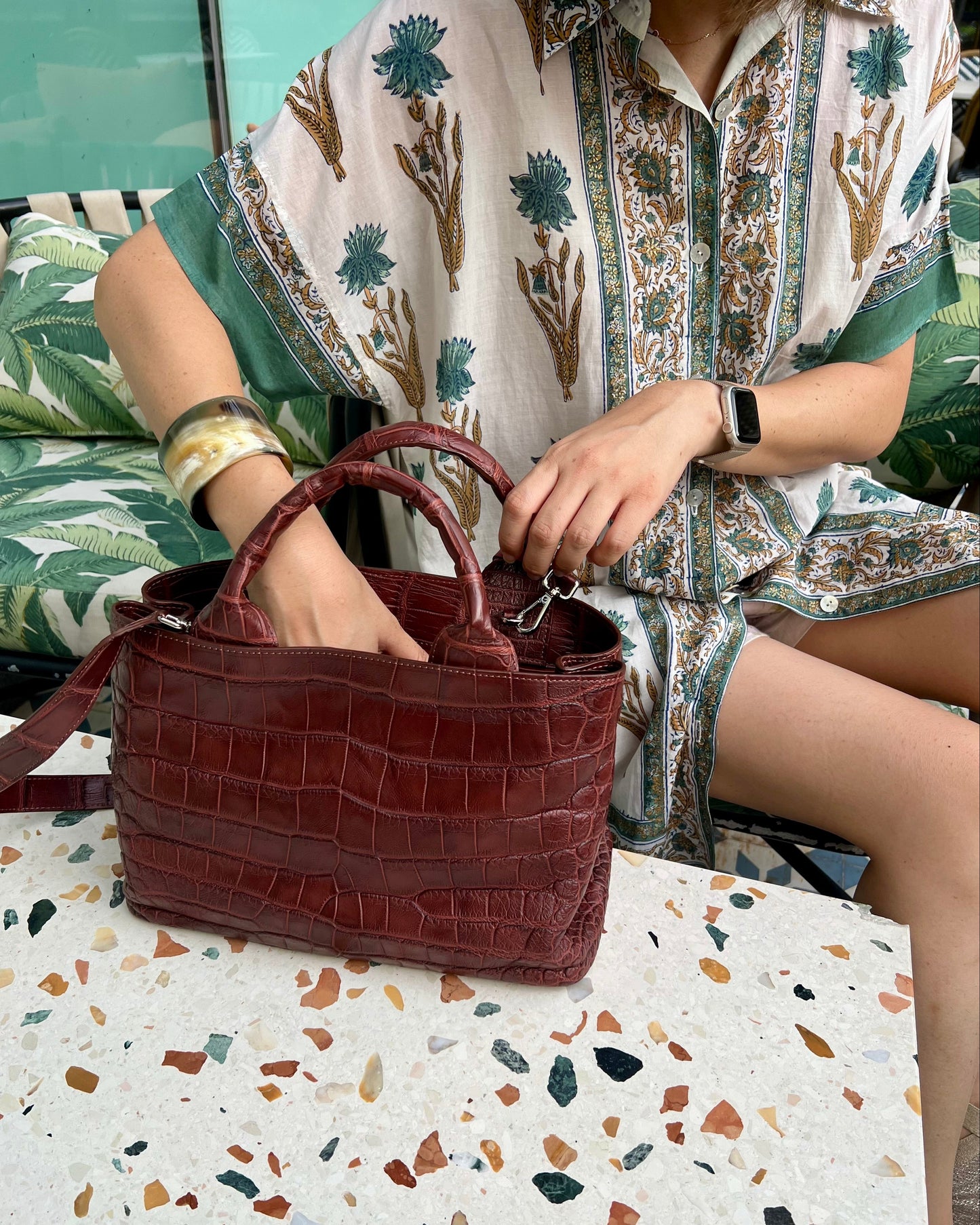 Person holding a brown handbag on a terrazzo-patterned floor.