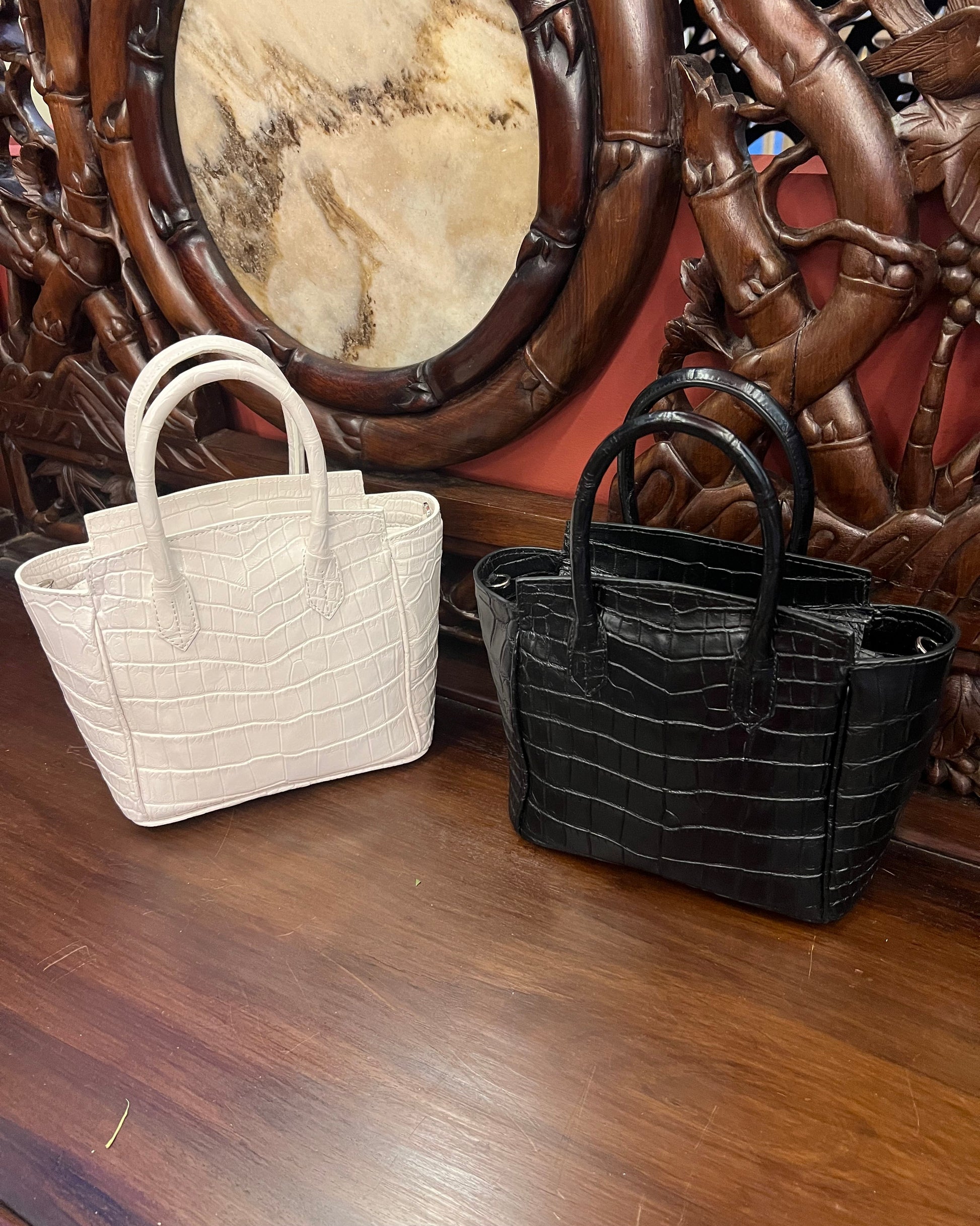 Two handbags, one black and one white, on a wooden surface with intricate carvings.