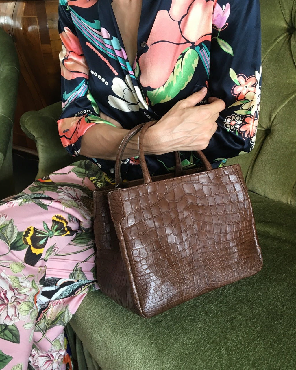 Person holding a brown handbag on a green couch with floral-patterned clothing.