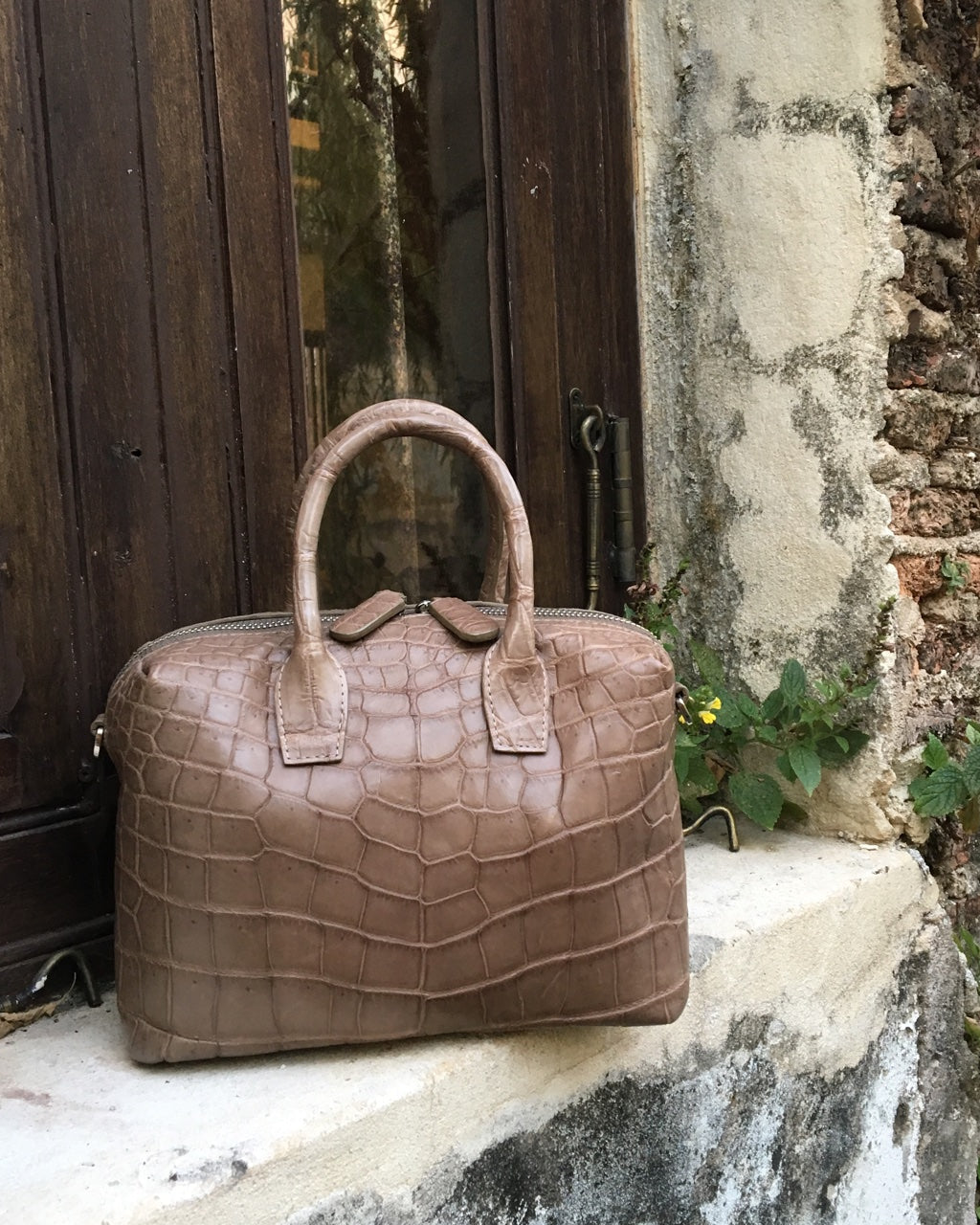 Brown textured handbag on a stone ledge with a rustic wall and door in the background