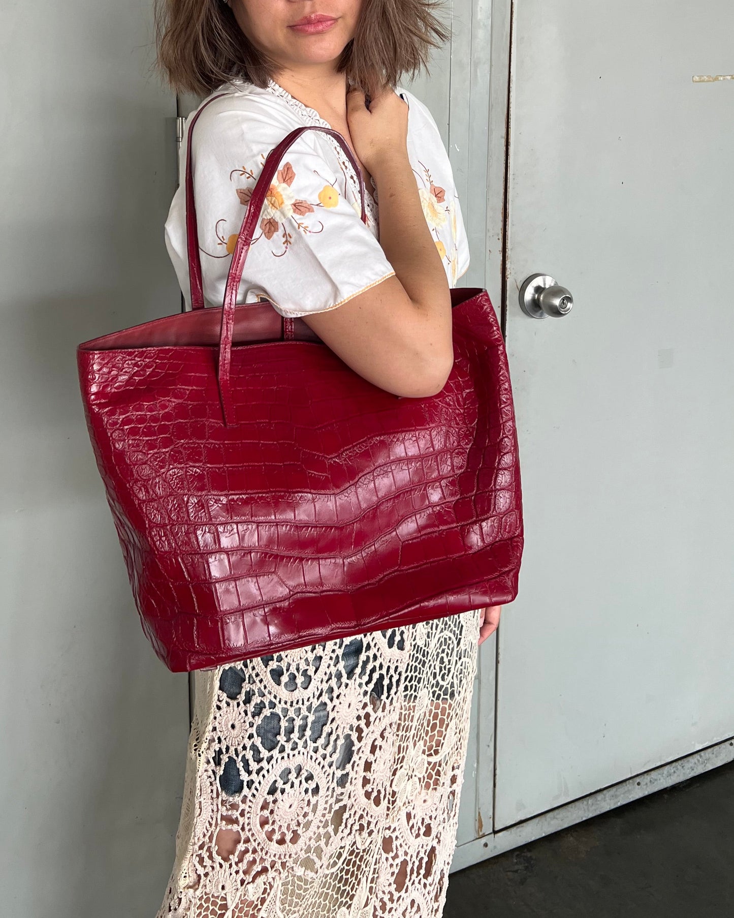 Person holding a red handbag in front of a gray door with yellow signs.