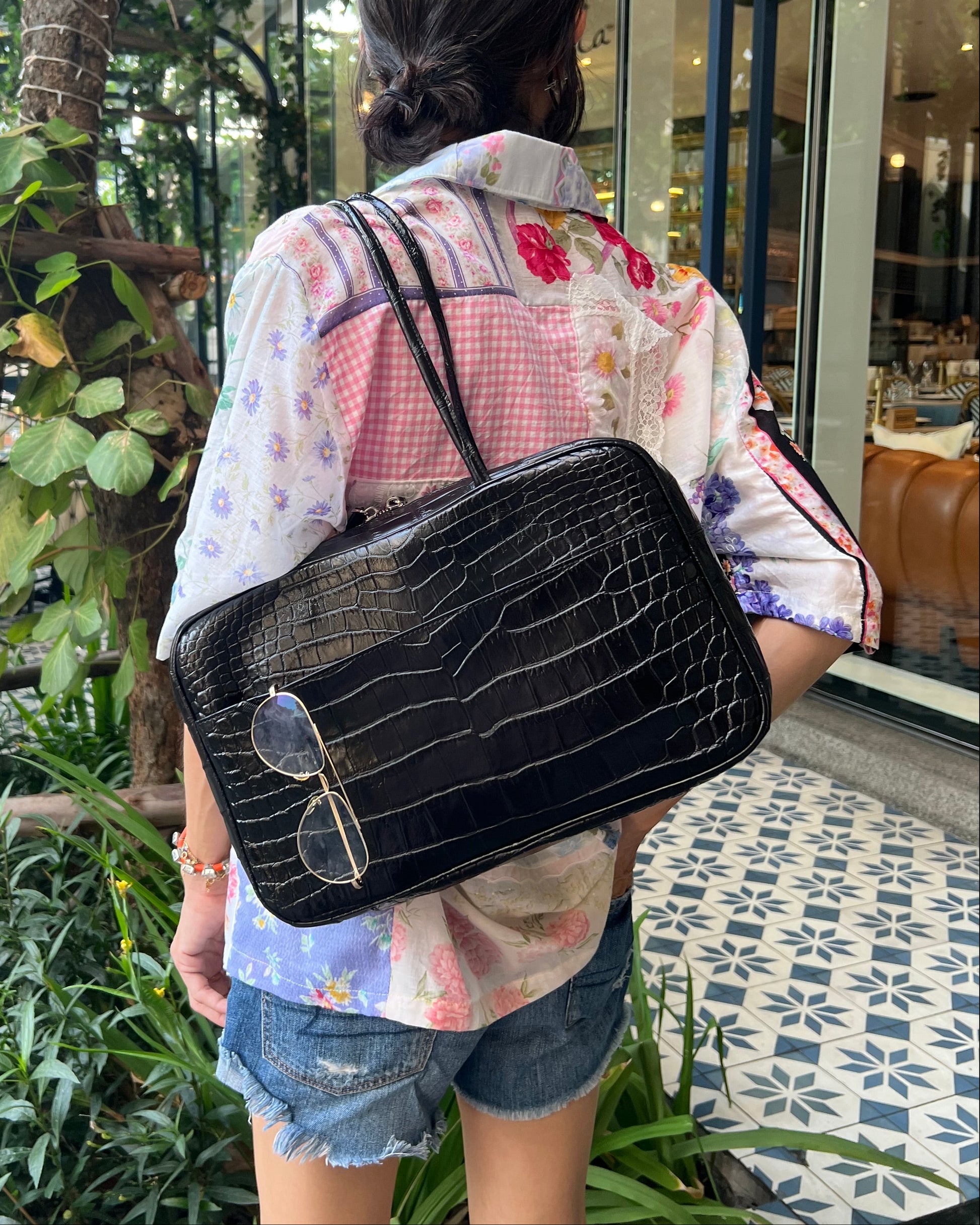 Person holding a black textured bag with plants and a building in the background