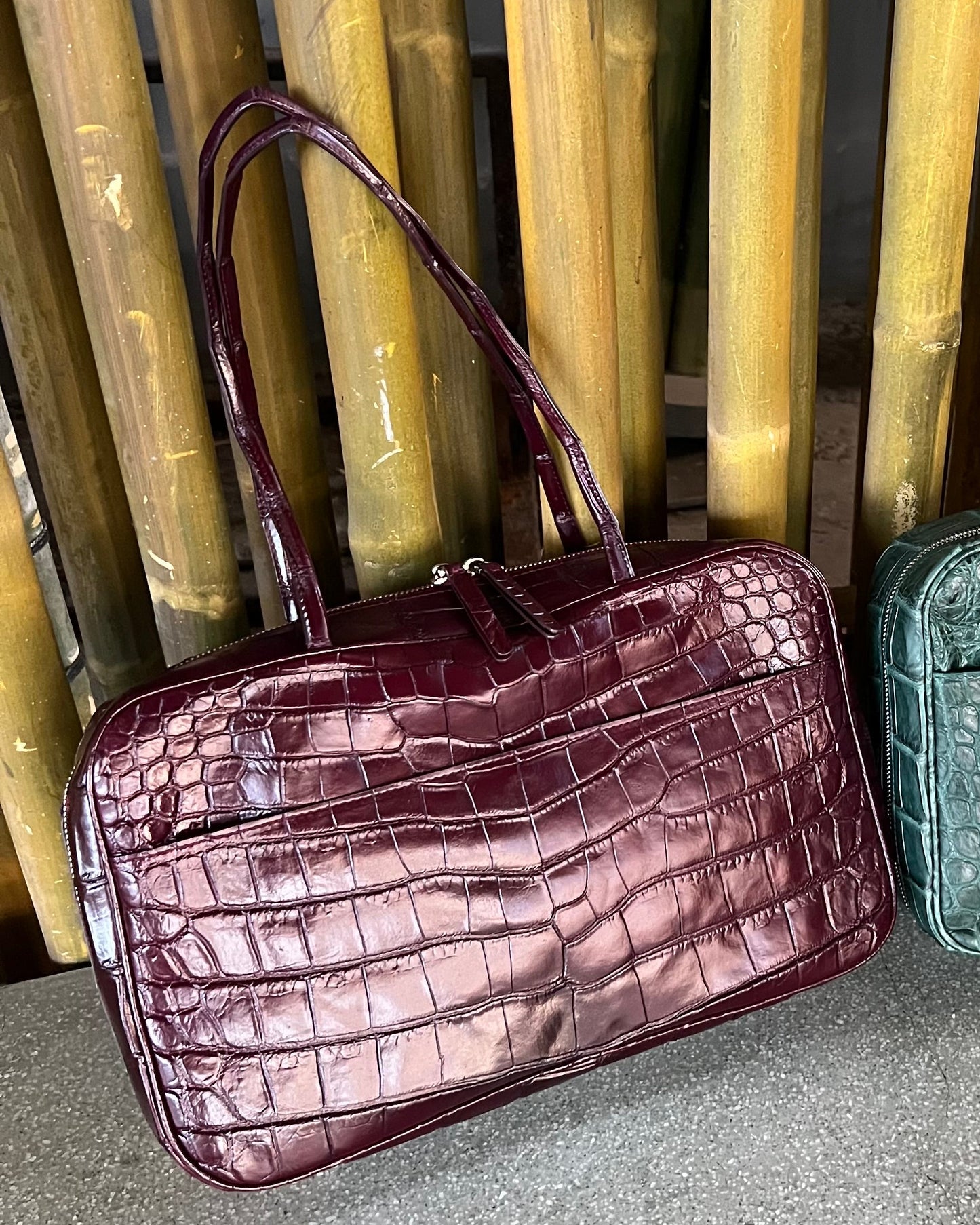 Two handbags, one purple and one green, against a bamboo background.